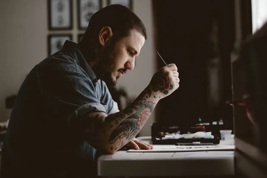 An artist drawing at the desk by the window, flash pinned on the wall behind.
