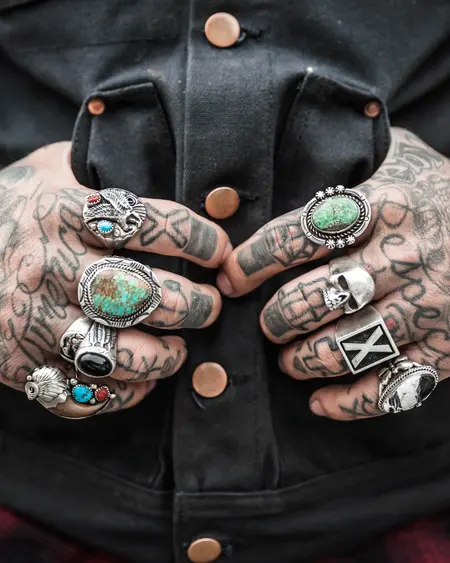 Two hands covered in small tattoos, under heavy silver rings.